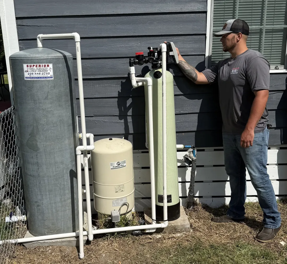 Superior technician programming the control head of a newly installed water filtration system and iron separator beside a pressure tank