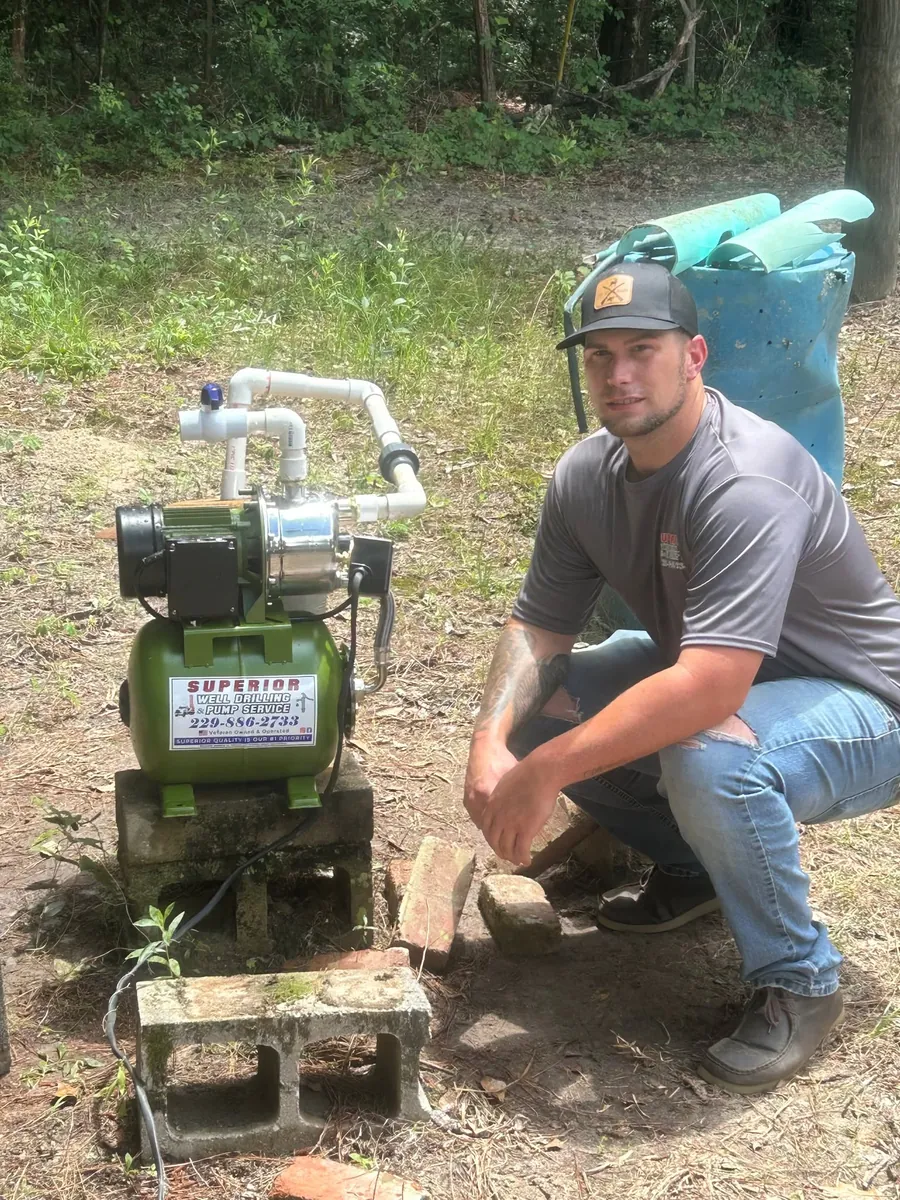 A Superior crew member kneeling beside a small green water pump installed on blocks at a food plot