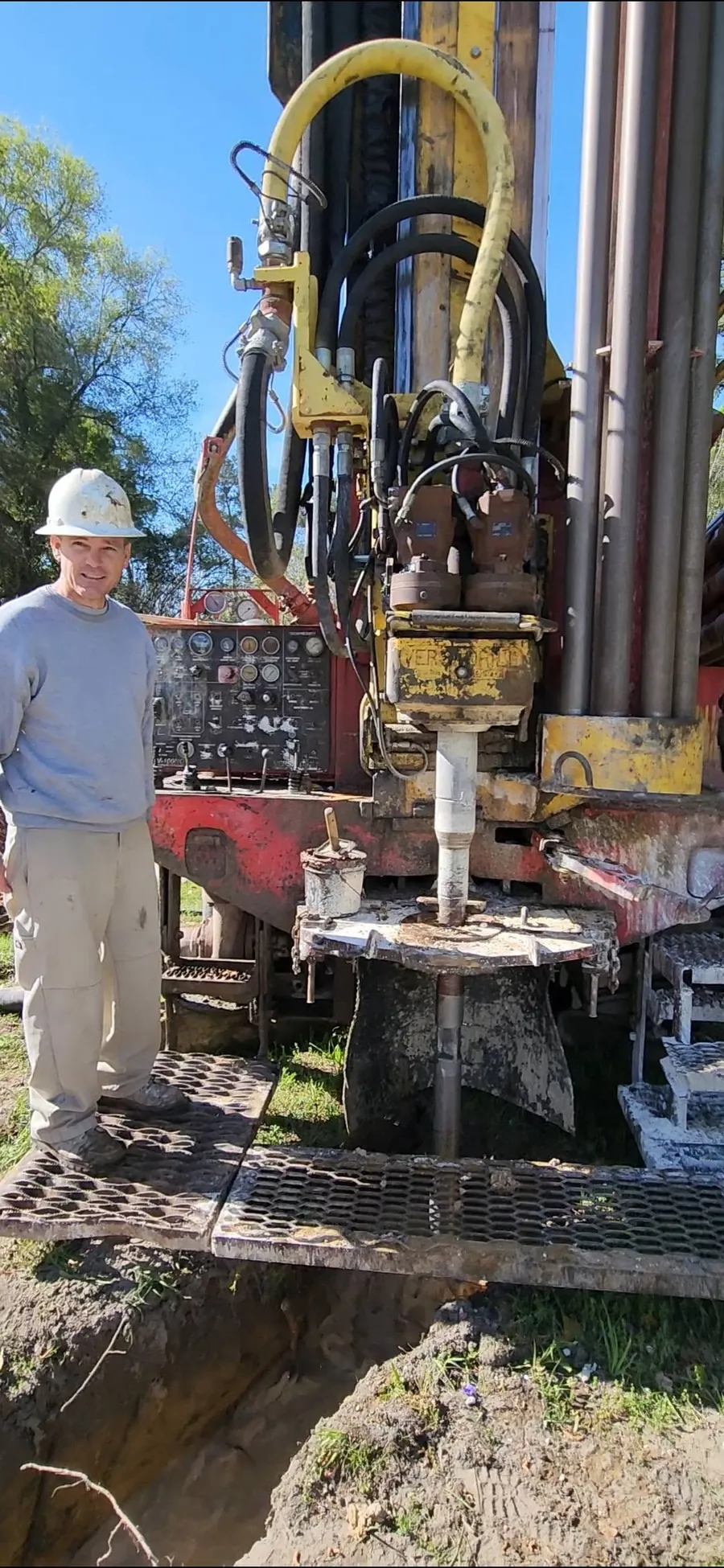 A Superior Well Drilling driller in a hard hat standing on the platform of the drill rig, with the drill pipe going down into the ground