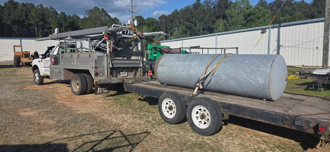 A large galvanized well tank strapped to a flatbed trailer behind a Superior service truck